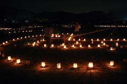 夜の周囲が暗い中で多くのろうそくの灯が入れ物に入って綺麗に見えている写真