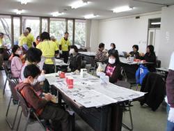 机が置かれた部屋で多くの人が石鹸づくりの講座を受けている写真