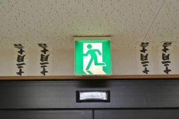 非常口誘導標識の両脇に各二枚ずつ貼られた魔よけ札の写真