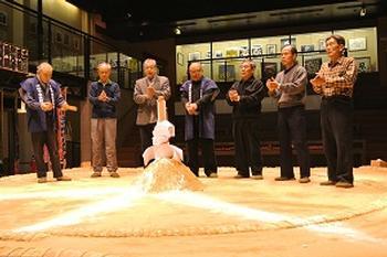 土俵祀りにて、盛り砂の上に供された御幣を前に拝礼を行うけはや相撲甚句会会員の写真