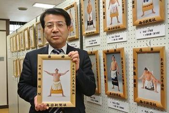 並べてパネル展示されているミニチュアの優勝額とその前で平成二十六年九月場所の優勝額を持つ男性の写真