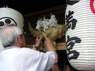 頭屋の玄関の軒先に御幣を刺したしめ縄を打ち付けている男性の写真
