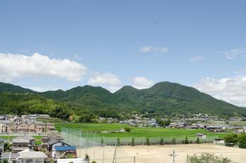 青空のもとグラウンドと住宅があり後ろに山々が写っている写真