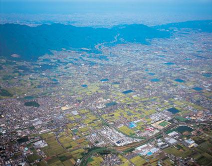 奥に山が見え、手前に畑や家屋が見える、上空から撮影した葛城市の写真