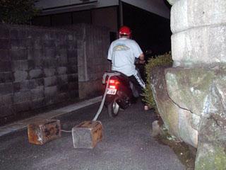 まだ日の上っていないなか石油缶を曳いたバイクが小路を進んでいく様子の写真
