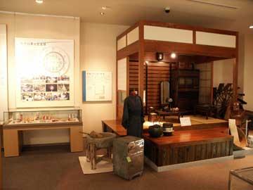 右側に板間と畳の室内を再現した展示場所と、左側に壁面展示とガラスケースが置かれた民具の展示風景の写真