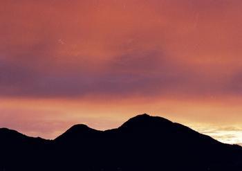 赤く焼けている雲がかかった空に黒いシルエットを見せる二上山の写真