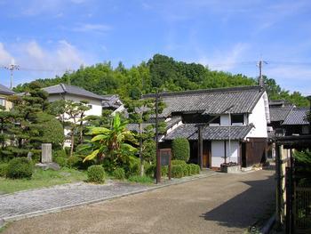 緑の木々が並ぶ明るい庭と、その中に立つ句碑の写真