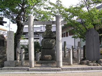 當麻蹶速の塚を示す石碑の奥の木陰に五輪塔がある写真