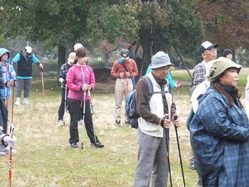ノルディックウォークのためのポールを持って公園の芝生に集まっている参加者達の写真