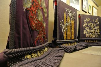 紫色に、それぞれ異なる刺繍が施された3枚の化粧まわしが並べて展示されている写真