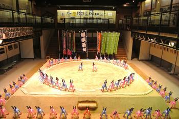 館内の土俵に配されたビニール鹿の展示風景の写真。たくさんのビニール鹿が土俵下・俵周り・仕切り線の各所に整然と並んでいる様子が確認できる