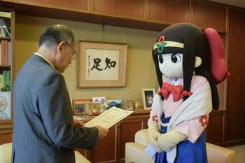 葛城市マスコットキャラクター蓮花ちゃんが阿古和彦市長より消費者教育推進大使の委嘱状を授与されている写真