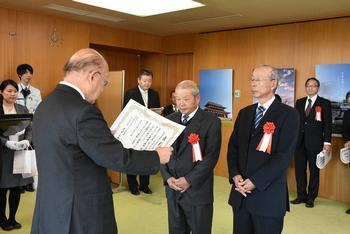 平成29年度奈良県観光事業功労者表彰式にて観光名所の写真が並ぶ部屋の中で、表彰状が読み上げられている写真