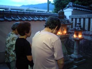 正面の石灯篭に灯がともされた本殿を参拝者たちの写真