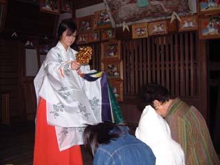 拝殿の中で正座する参拝者とその頭上で神楽鈴を使ってお祓いをする巫女の写真