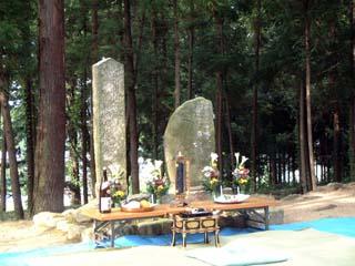 前に置かれた机の前に御神酒や供え物が並べられている2つの墓碑の写真