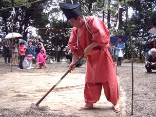 境内にて田起こしした田んぼで鍬を使って畔づくりの神事を行う氏子総代の写真