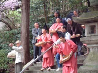 石段の登り口から餅撒きをする氏子総代たちの写真