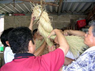 複数の男性がしめ縄の縄を編んでいる写真