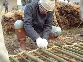 竹杭を藁縄によってつなぎ合わせてスダレ状に組んでいく作業の写真
