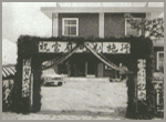 建物の手前に、四角いリボンがかけられ文字が書かれたアーチがある白黒写真