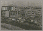 手前にグラウンドがある、横に長い白鳳中学校新校舎の外観の白黒写真