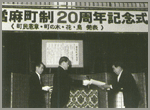 「當麻町制20周年記念式」と書かれた幕の下で、授与式が行われている白黒の写真