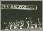 ステージ上で人々が楽器を演奏していて、指揮者が指揮をしている白黒の写真