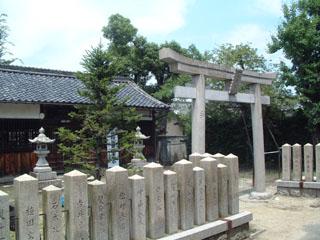八幡神社にて、石づくりの鳥居の奥に石の燈篭や緑の木々とともに社殿がある写真