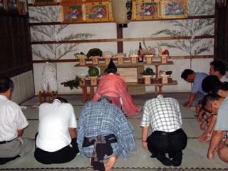 拝殿にて烏帽子姿の人と集まった人々が祈りをささげている様子の写真