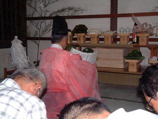 拝殿にて烏帽子姿の人が祝詞を上げている様子の写真