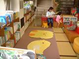 床にマットレスを敷き、周囲を本棚やソファーで仕切った窓辺にある乳幼児コーナーの写真