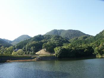 湖に隣接した木々で覆われた鳥谷口古墳と山々の写真