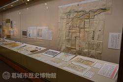 台の上や壁面に様々な資料が飾られた展示風景を右斜め前から撮影した写真