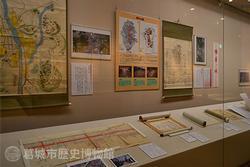 台の上や壁面に様々な資料が飾られた展示風景を左斜め前から撮影した写真