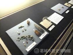 台の上の正方形のプレートに並べられた大小様ざまな形の石材、石器の展示風景の写真