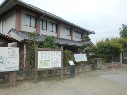 當麻寺の説明書きと植木の奥にある二階建ての當麻地区公民館の写真